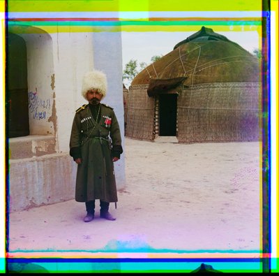 Een gewapende man in uniform staat naast een gebouw met een joert op de achtergrond, Rusland, 1915 door Sergey Prokudin Gorsky